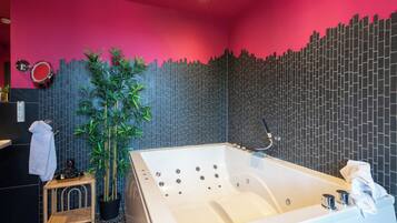 Een moderne badkamer met een groot bad, een potplant en een opvallend wandontwerp.