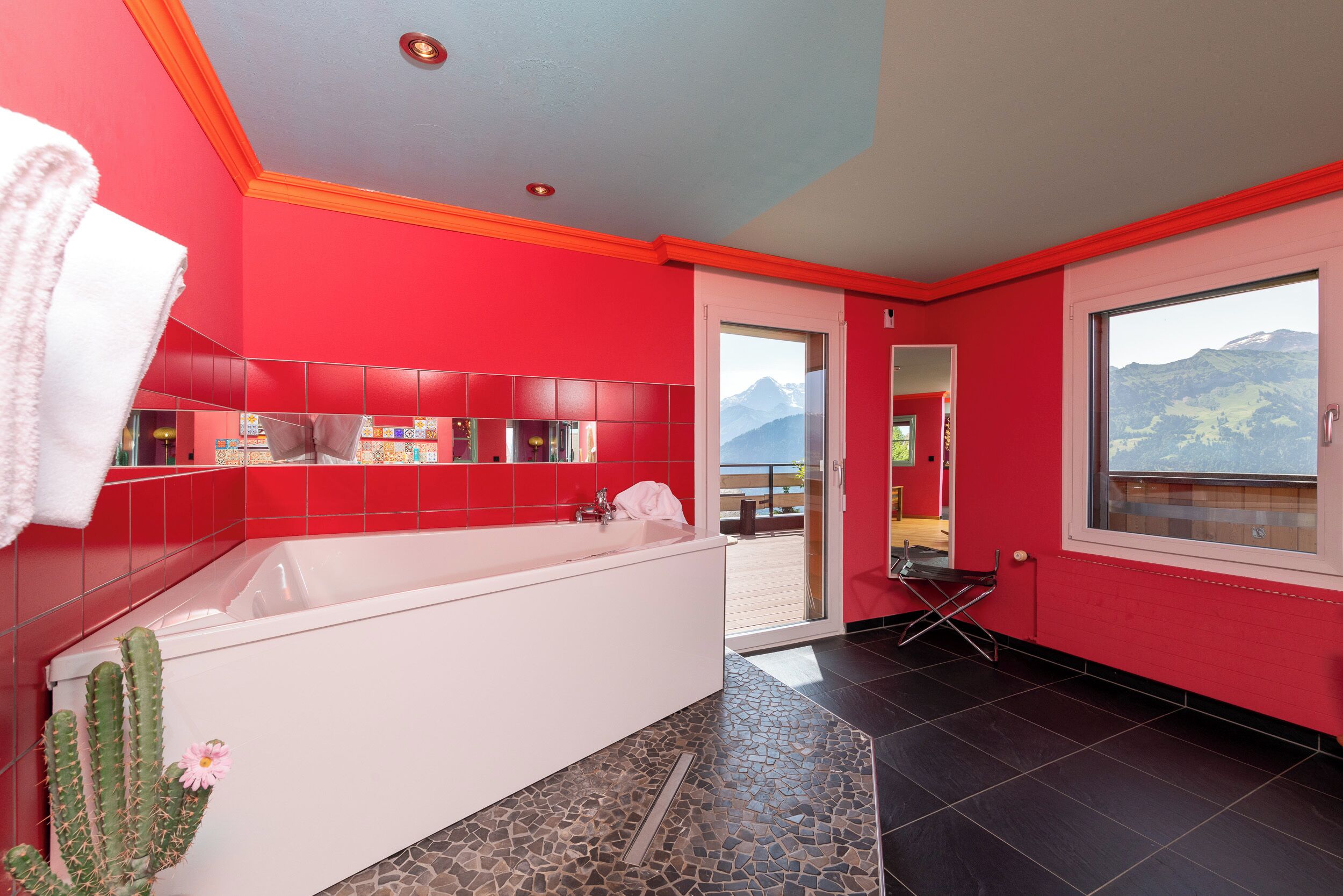 Un baño moderno con una bañera grande, paredes rojas y vistas a las montañas a través de una ventana.