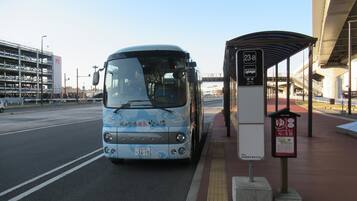 A bus stop with a shelter, a bus, and a parking structure in the background.