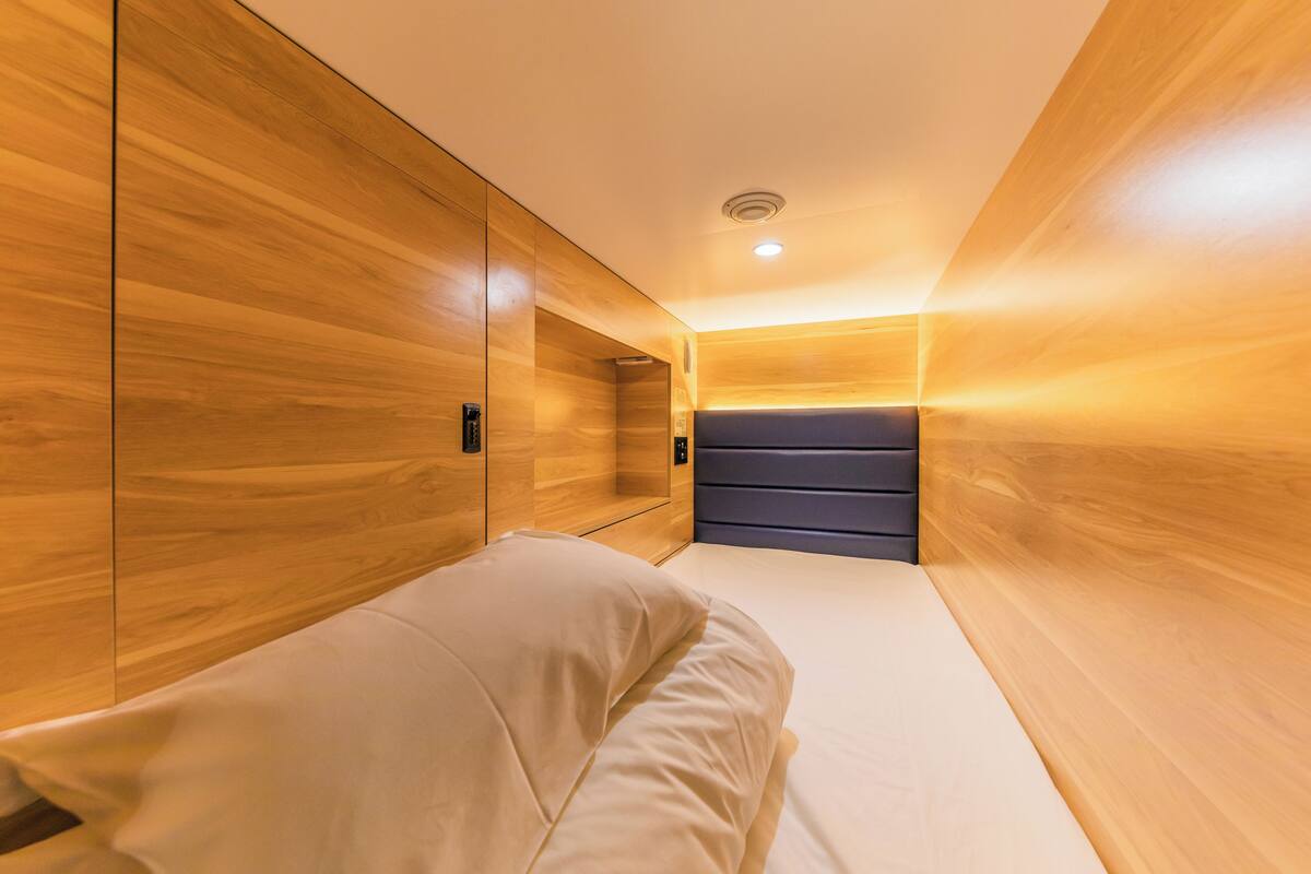 A modern hotel room with wooden paneling, a bed with white linens, and a built-in wardrobe.