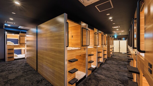 A row of bunk beds with wooden walls and metal railings, carpeted floors, and ceiling lights. - Soranoyu Spa Resort (Shibayama)