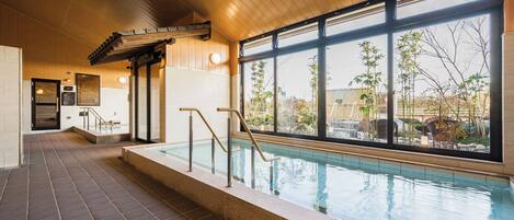 An indoor swimming pool with a view of the outdoors, a tiled floor, and a wooden ceiling.