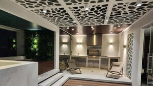 Ein moderner Außenbereich mit Küche, inklusive Grill, Sitzgelegenheit und dekorativer Decke.