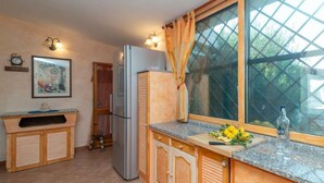A compact kitchen with wooden cabinets, a built-in refrigerator, a sink, and a window with curtains. - Vacation home Fusco by Interhome (Olbia)