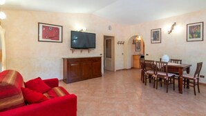 A living room with a red sofa, a TV mounted on the wall, and a dining area with a table and chairs. - Vacation home Fusco by Interhome (Olbia)
