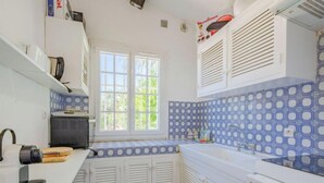 A compact kitchen with white cabinets, a blue patterned backsplash, and a window providing natural light. - Le Clos d´Estelle by Interhome (La Garde Freinet)