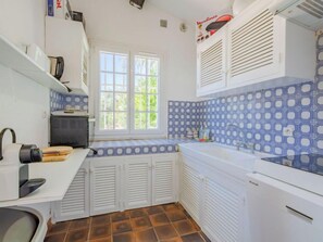 Una cocina compacta con armarios blancos, un salpicadero azul con estampado y una ventana que proporciona luz natural.