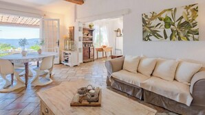 A cozy living room with a sofa, a coffee table, and a bookshelf. There is a view of the outdoors through a glass door. - Le Clos d´Estelle by Interhome (La Garde Freinet)