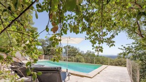 A swimming pool with a view of the sea, surrounded by a concrete deck and a covered area with a chair and umbrella. - Le Clos d´Estelle by Interhome (La Garde Freinet)