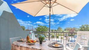 Ein Balkon mit Esstisch, einem großen Sonnenschirm und Blick auf einen Parkplatz und Bäume.