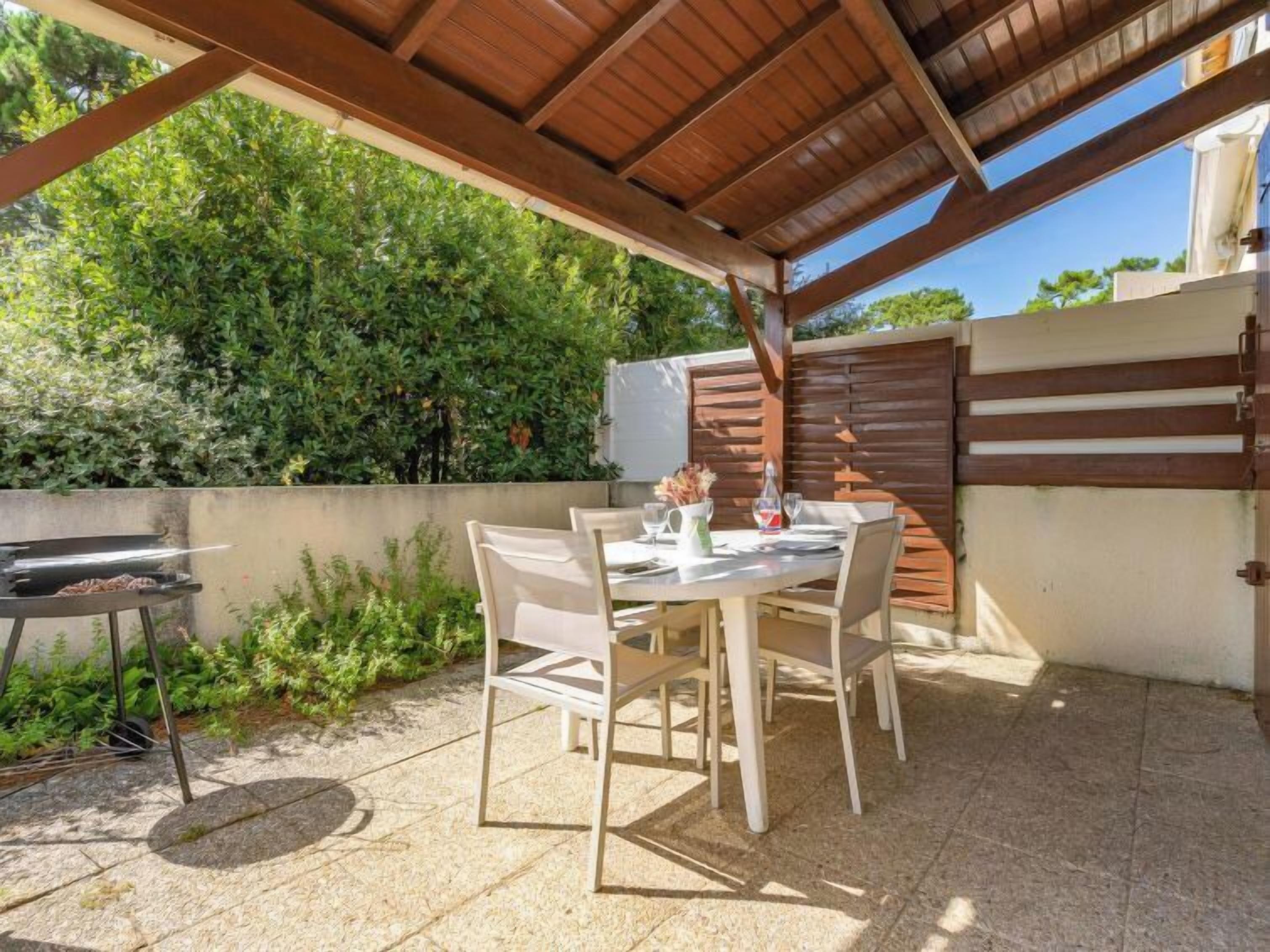 An outdoor patio with a table and chairs, a grill, and a wooden fence.