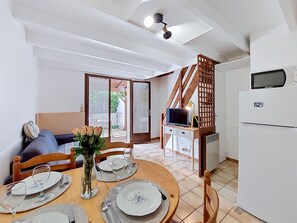 Spiseområde med et bord til fire personer, en sofa, et fjernsyn og et køleskab.
