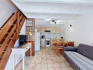 En kompakt opholdsstue med tekøkken, spiseplads og trappe op til en etage.