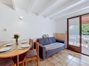 Et spiseområde med et træbord dækket til fire personer, en blå sofa og en skydedør, der fører til en udendørs terrasse.