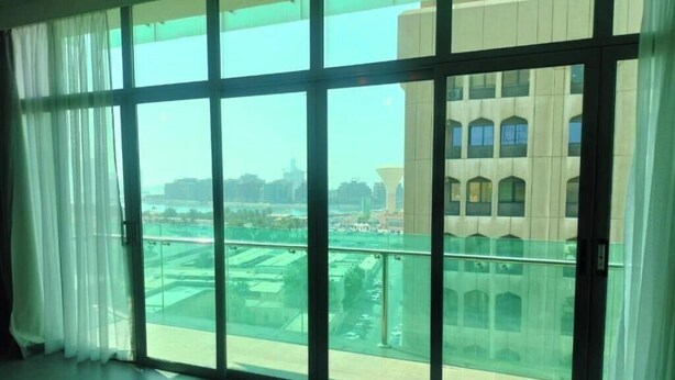 A room with large floor-to-ceiling windows, a view of a cityscape, and a modern building in the background. - CITY POINT HOTEL (Manama)