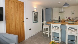 A modern kitchen with a central island, white chairs, and a dining table. - Kestrel (Malpas)