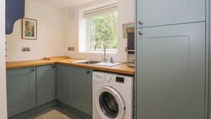 A compact kitchen with a washing machine, wooden countertop, and a window with a view of greenery. - Kestrel (Malpas)