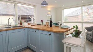 A kitchen with a wooden countertop, blue cabinets, a sink, and a dining area with a chair and table. - Kestrel (Malpas)