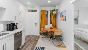 A modern kitchen with white cabinets, a coffee machine, and a dining area with a round table and chairs. - Cozy Oasis in the heart of Capitol Hil (Seattle)