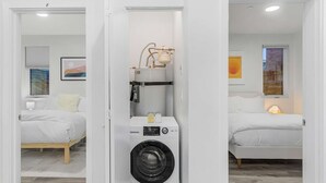 A compact room with a built-in washer and dryer, two beds, a window with a view, and a painting on the wall. - Cozy Oasis in the heart of Capitol Hil (Seattle)