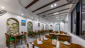 A spacious dining area with wooden tables and chairs, a ceiling fan, and artwork on the walls. - Cat Ba Green Pearl Hotel (Hai Phong)