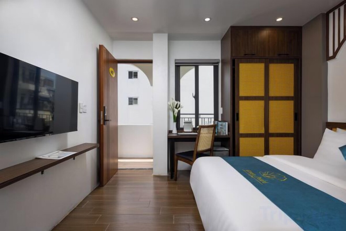 A hotel room with a bed, a desk, a television, and a view of the outside.