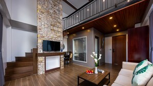 A modern living room with a stone accent wall, wooden flooring, a sofa, a coffee table, and a staircase leading to an upper level. - Cat Ba Green Pearl Hotel (Hai Phong)