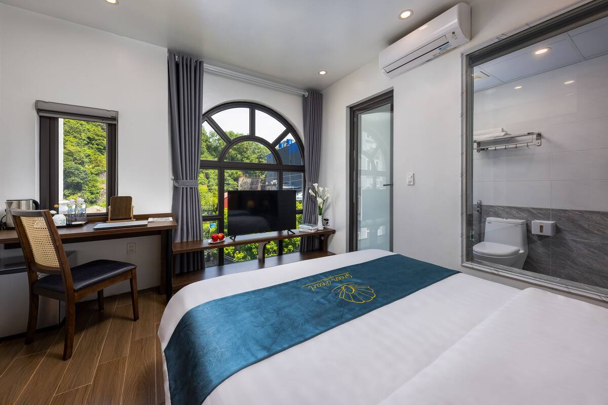 Een hotelkamer met een bed, een bureau met een computer, een televisie en uitzicht op groen buiten.
