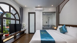 A hotel room with a large window, a bed with a blue bed runner, a nightstand with a lamp, and a view of the outside. - Cat Ba Green Pearl Hotel (Hai Phong)