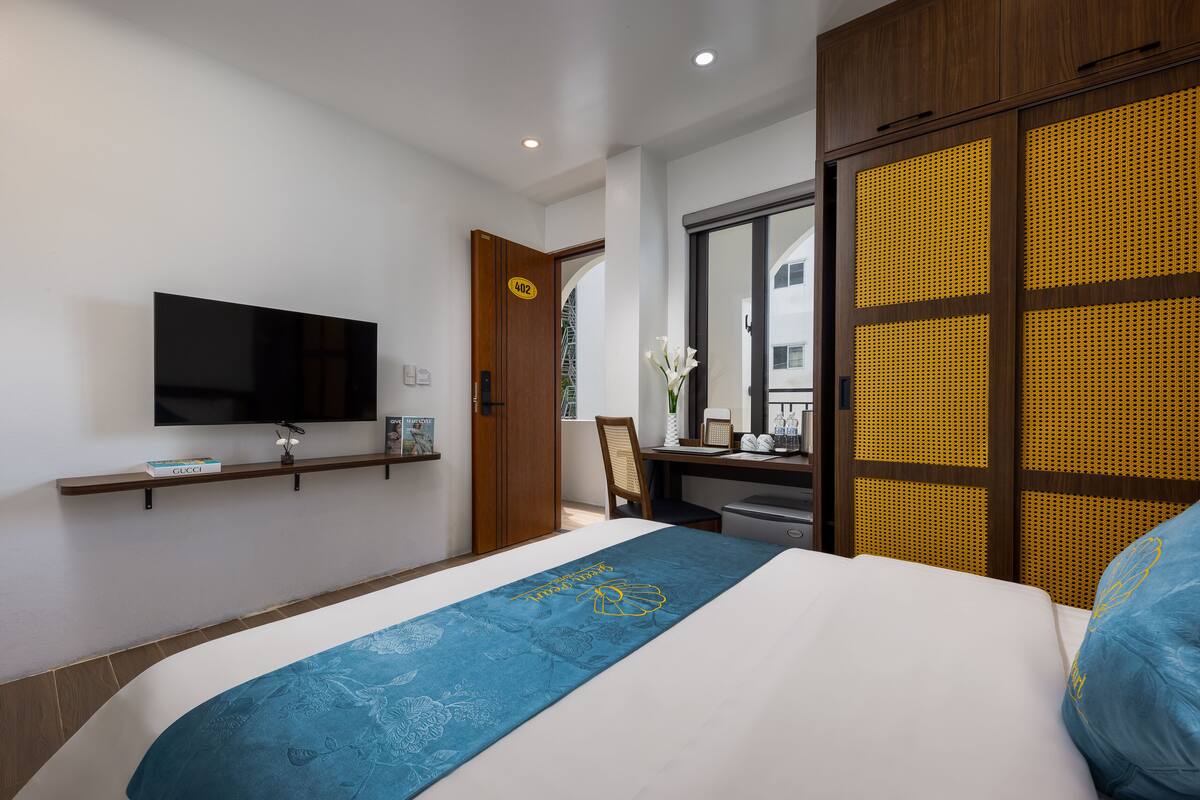 Een hotelkamer met een bed, een aan de muur bevestigde televisie, een bureau met een computer en een kledingkast met een deur met een geel patroon.
