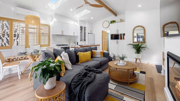 Een moderne woonkamer met een grijze bank, een eethoek met een glazen tafel, en een keuken op de achtergrond.