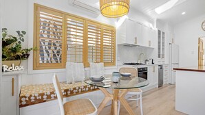 Een moderne keuken met witte kasten, een glazen eettafel en een houten bank.