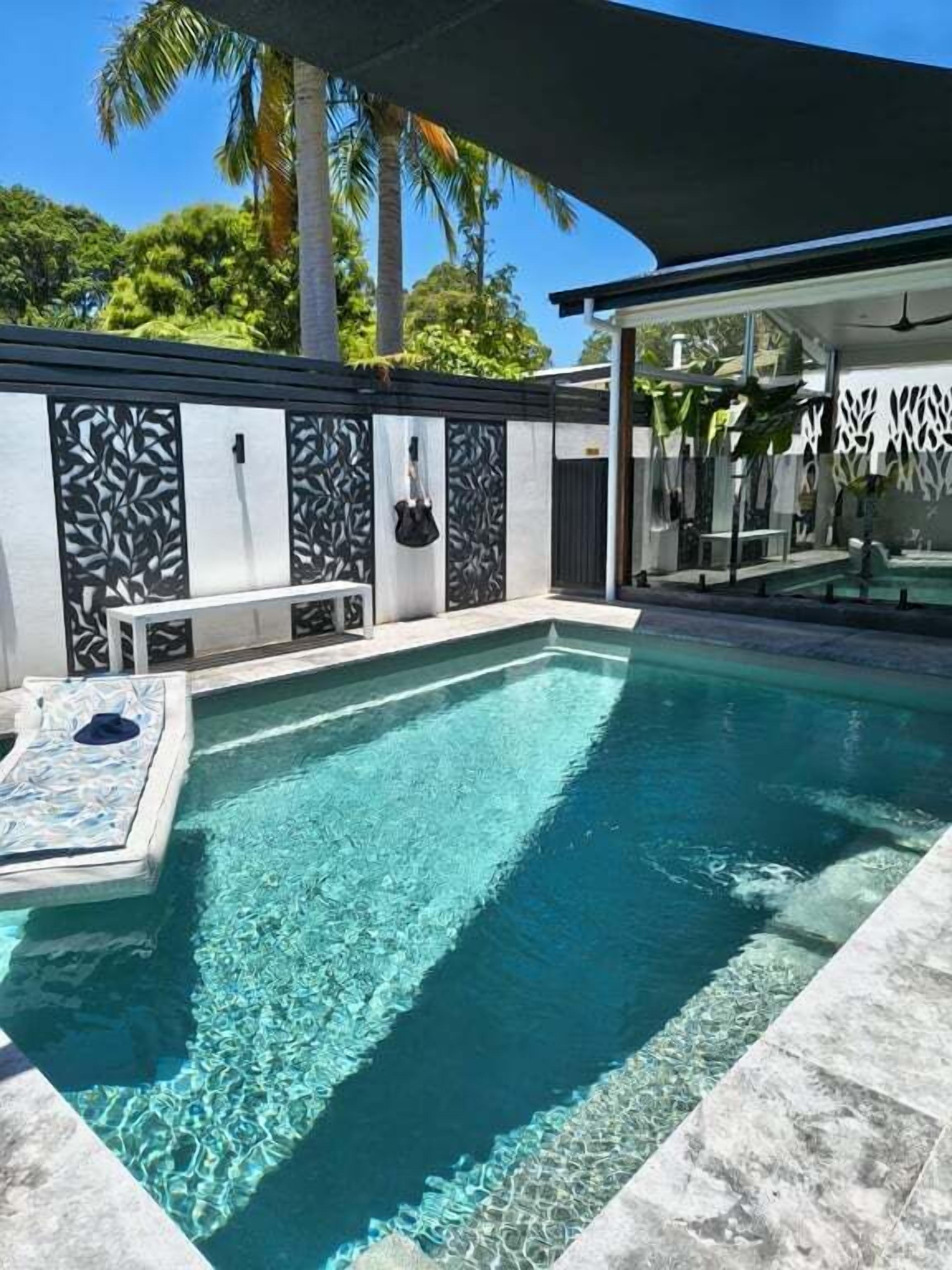Una piscina con agua cristalina, rodeada por una zona moderna junto a la piscina, con un banco y un área de estar cubierta.