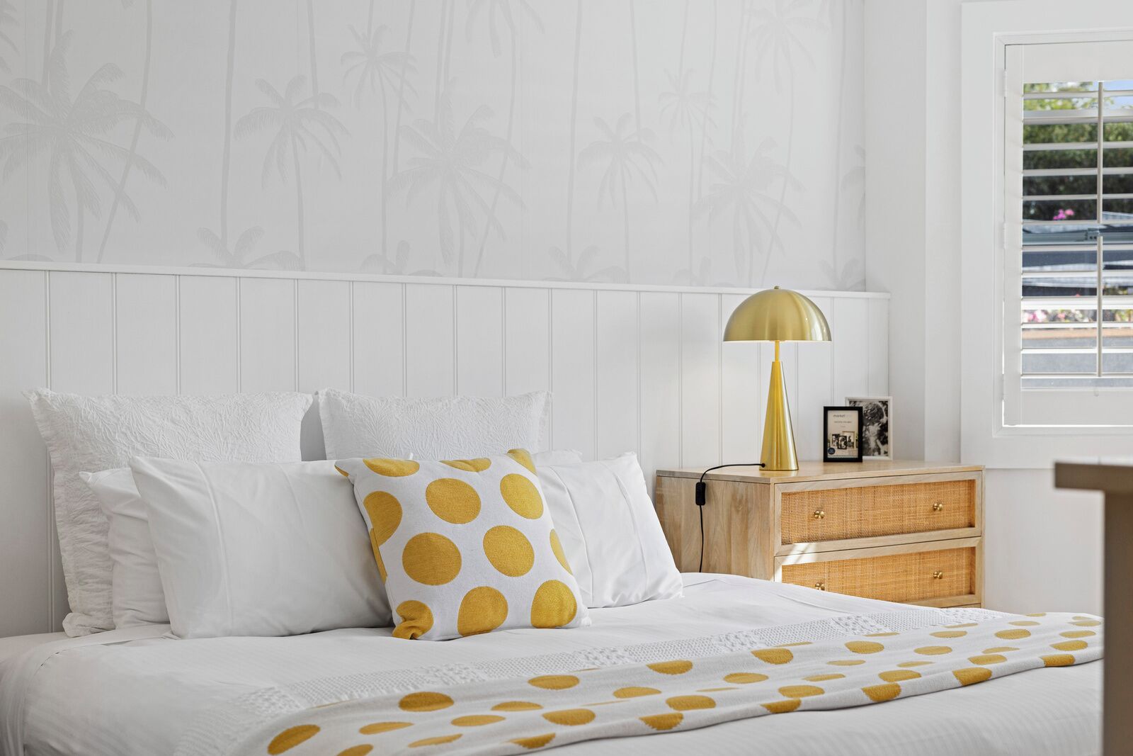 Et pænt opredt soveværelse med seng, puder, en senget lampe og et natbord.