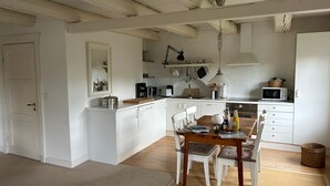 A compact kitchen with white cabinetry, a dining table with chairs, and a hanging light fixture. - Teyhörn in the Pilsumer Hof from 1551 (Krummhörn)