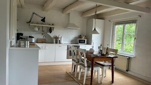 A kitchen with white cabinets, a wooden dining table, and chairs. There is a window with a view of greenery outside. - Teyhörn in the Pilsumer Hof from 1551 (Krummhörn)
