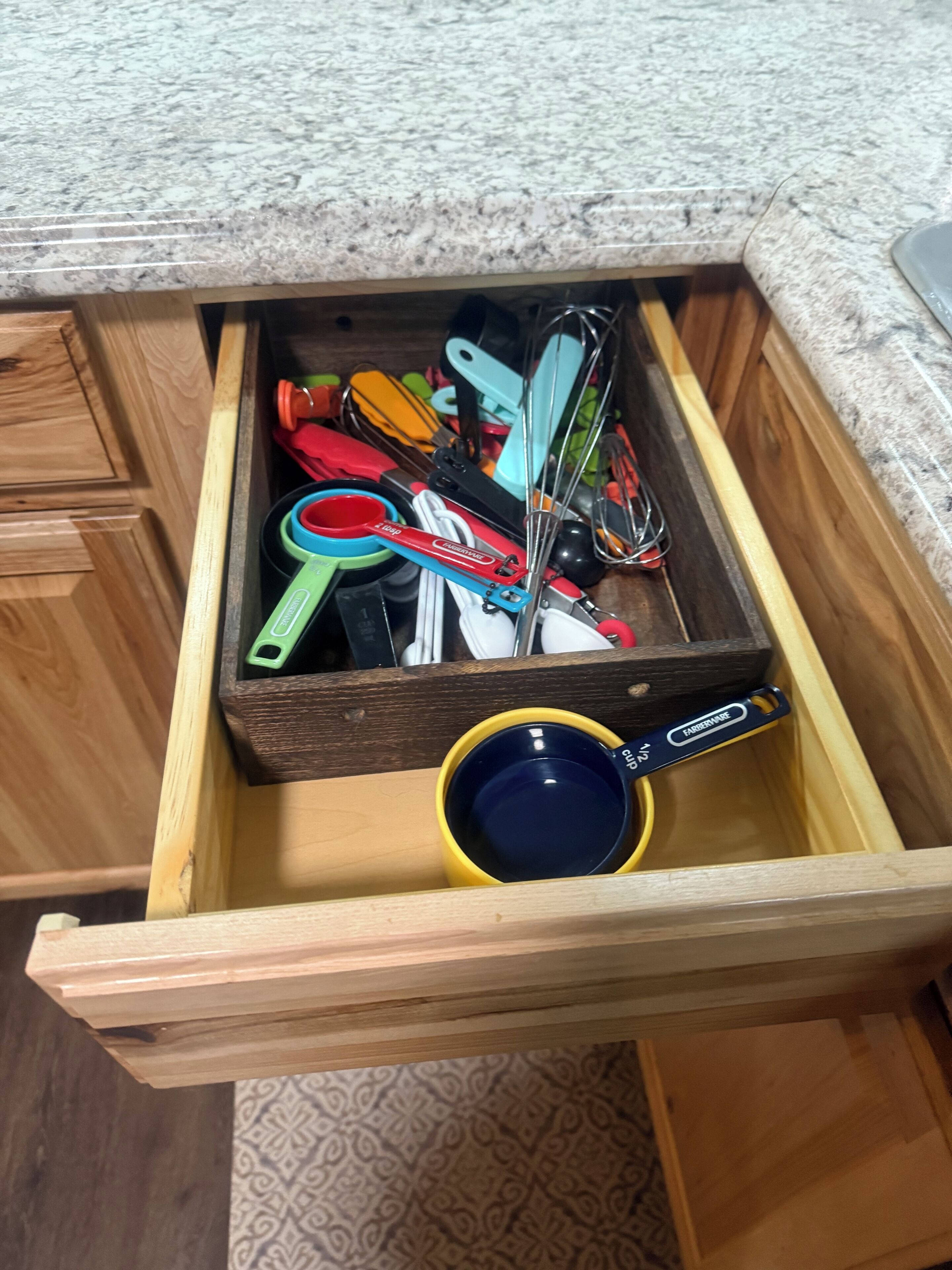 A drawer with various kitchen utensils and a yellow mug.