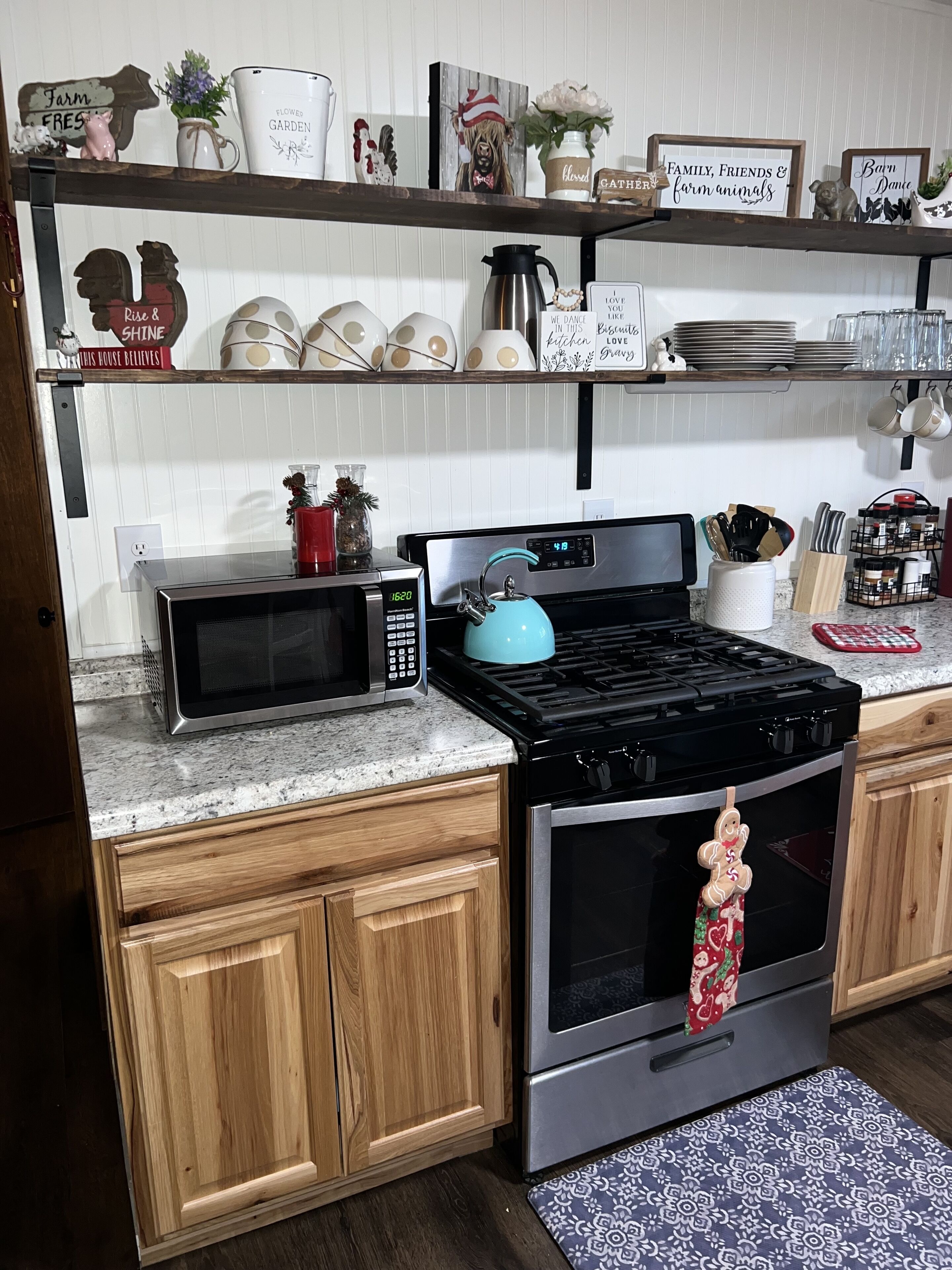 A kitchen with a microwave, stove, oven, wooden cabinets, and various kitchen utensils and decorations on the shelves.