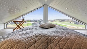 A bedroom with a large bed, a wooden table, and a view of a residential area through a skylight. - "Alea" - 800m from the sea by Interhome (Hjørring)