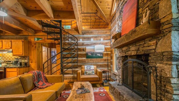 Un intérieur de chalet chaleureux avec une cheminée en pierre, un escalier en bois et un coin repas rustique.