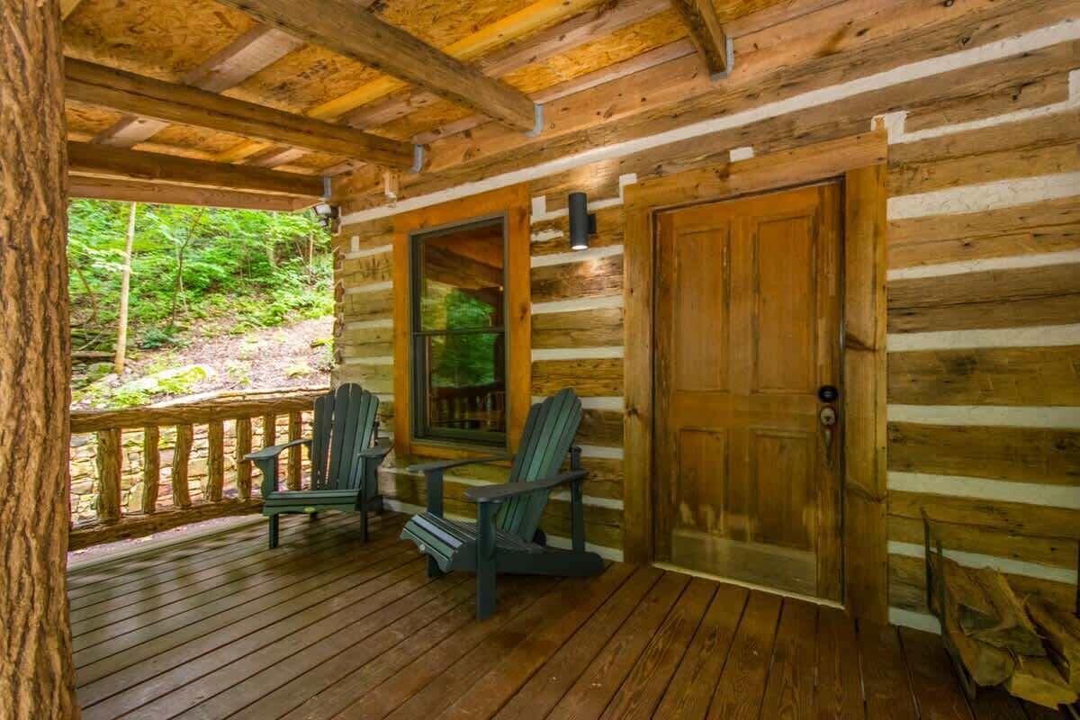 A log cabin with a wooden porch, two Adirondack chairs, and a door.