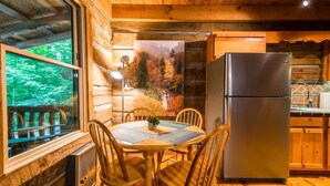 L’intérieur d’un chalet en bois comprend une table à manger, des chaises, un réfrigérateur et une fenêtre donnant sur une forêt.