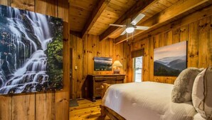 Une chambre dans une cabane en bois, avec un lit, un bureau et un ventilateur de plafond.