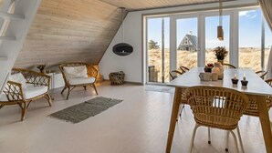 Ein modernes Interieur mit hohen Decken, großen Fenstern und einer Essecke mit Korbmöbeln.