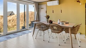 Ein Essbereich mit Tisch und Stühlen, einer Tür mit der Aufschrift 'SAGA' und Blick auf die Landschaft durch große Fenster.