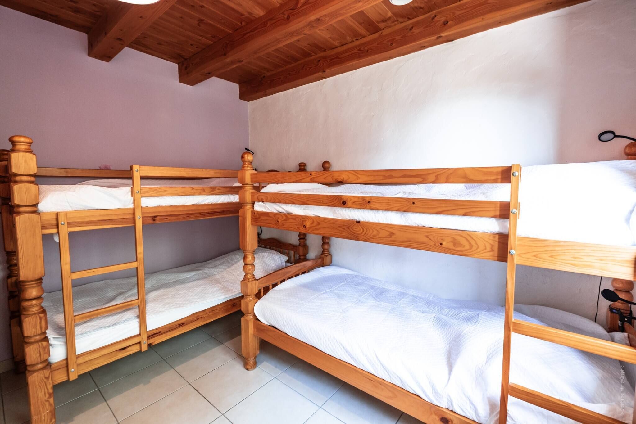 A room with three wooden bunk beds, white bedding, and a wooden ceiling.