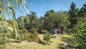 Een achtertuin met een houten speelconstructie, een kleine schuur en een tuin met verschillende planten en bomen.