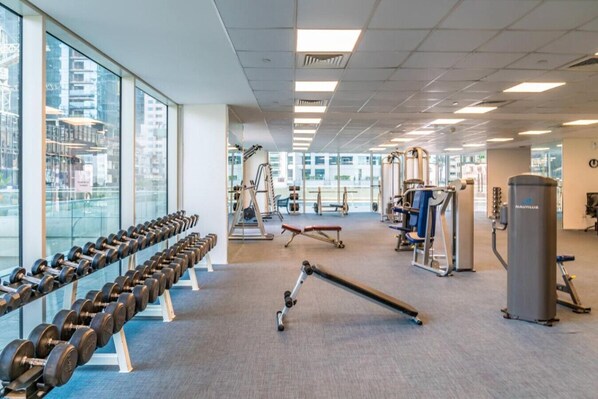 A gym with weightlifting equipment, cardio machines, and large windows offering views of the city. - Marina Heights - Unique One Bedroom (Dubai Marina)