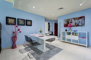 A modern dining area with a white table, black chairs, and a red vase with flowers. There is a white bookshelf with books and decorative items.
