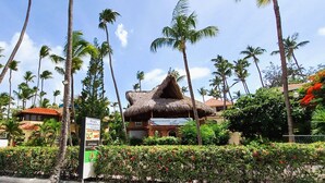 Un resort con una construcción de techo de paja, palmeras y un letrero que anuncia un restaurante y una pizzería.